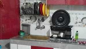 A kitchen with red and white cabinets, a sink, and various kitchen utensils and appliances. - Bushahri Homestay (Narkanda)