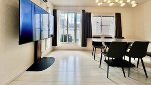A modern dining area with a large flat-screen TV, a dining table with chairs, and a ceiling light fixture. - COREHOTEL Ikebukuro (Tokyo)