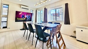 A modern dining area with a large TV screen, wooden chairs, and a table. - COREHOTEL Ikebukuro (Tokyo)