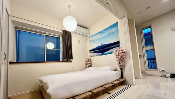 A modern bedroom with a bed, a window, a painting, and a vase of flowers. - COREHOTEL Ikebukuro (Tokyo)
