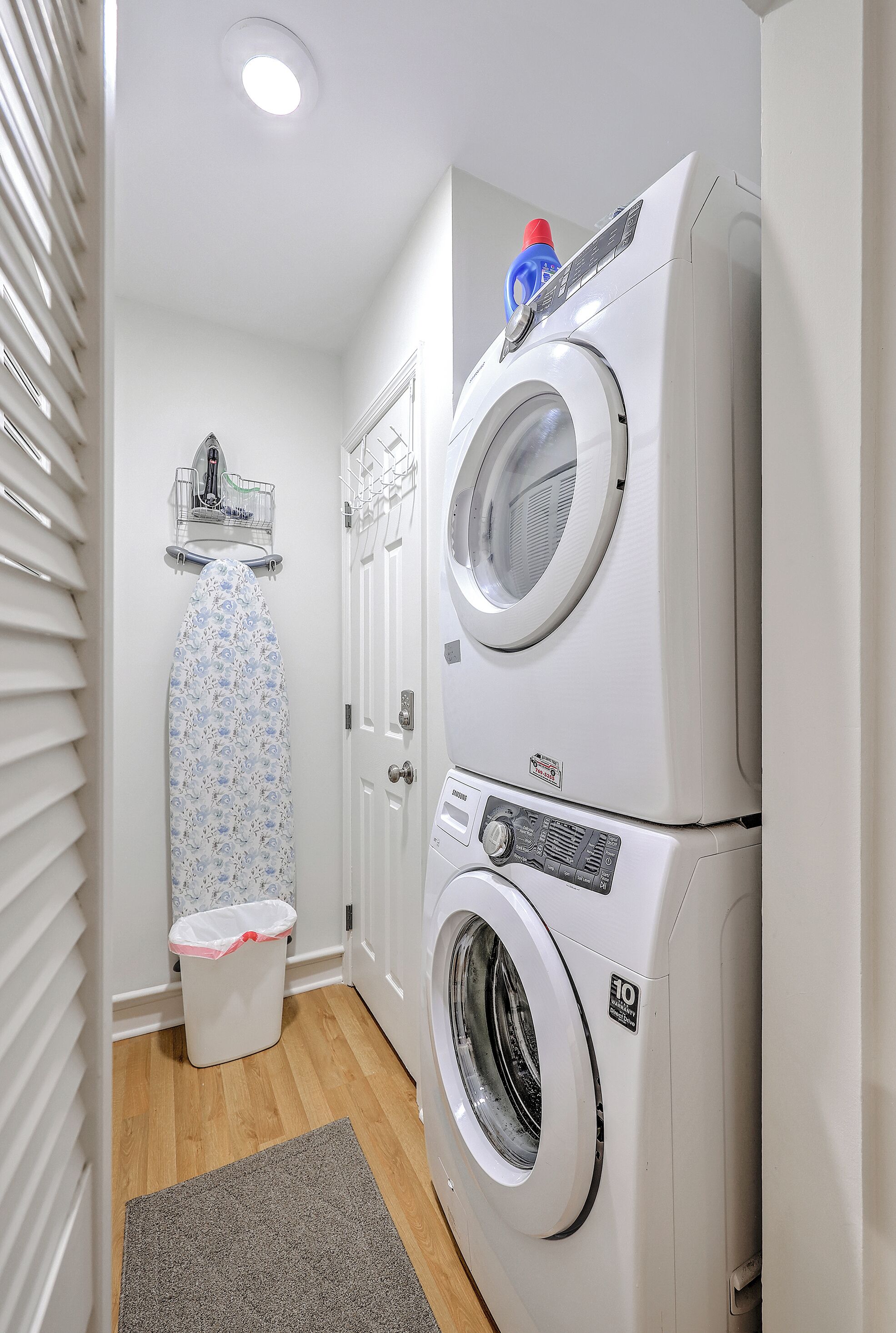 Un cuarto de lavado con dos lavadoras apiladas, un tendedero y un cubo de basura.
