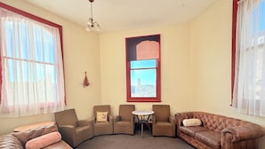 Una sala de estar con un sofá de cuero marrón, dos sillones, una mesita redonda y un ventanal con vista a un edificio.