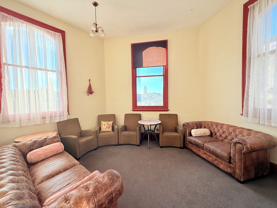 A living room with a brown leather sofa, two armchairs, a small round table, and a window with a view of a building.