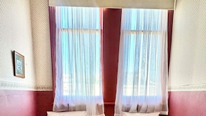 Habitación con dos camas, suelo de madera y ventana con cortinas traslúcidas.