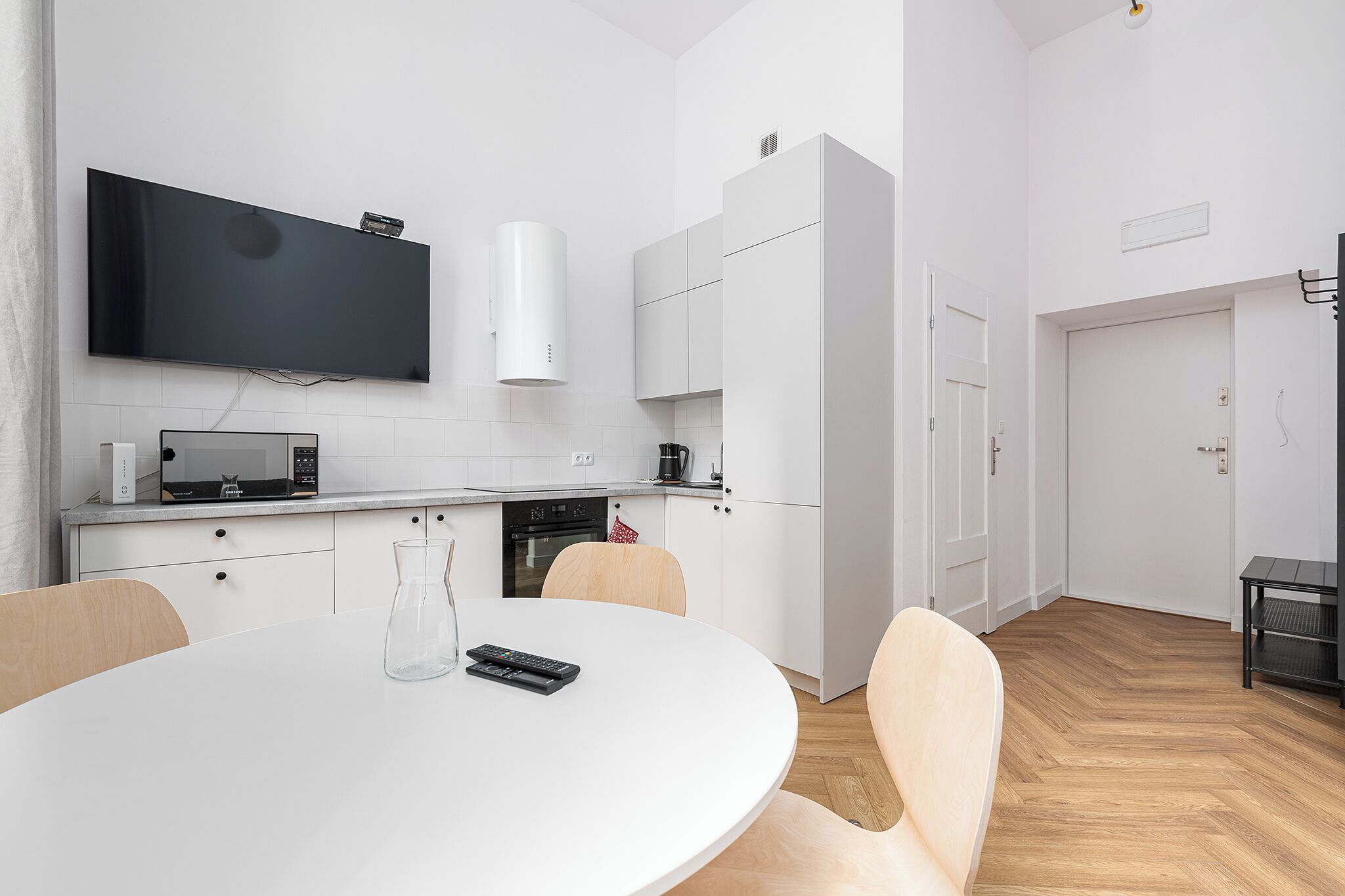 Una cocina moderna con televisor de pantalla plana, microondas y horno empotrado. Hay una mesa de comedor con sillas y un florero.