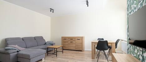 Un salon moderne avec un canapé d’angle gris, une table à manger en bois et un petit meuble en bois.