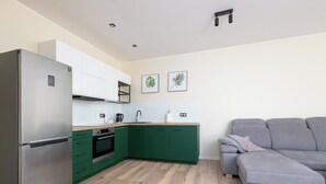 Eine moderne Küche mit grünen Schränken, einem Edelstahl-Kühlschrank und einem grauen Sofa im Wohnbereich.
