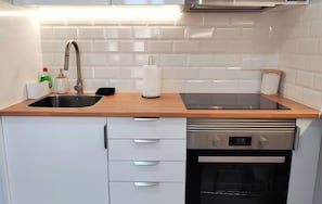A modern kitchen with a stainless steel sink, a built-in oven, and white tiled backsplash.