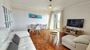 A modern living room with a sofa, TV, dining area, and a painting on the wall.