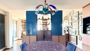A dining area with a round table, chairs, a chandelier, and a bookshelf in the background.