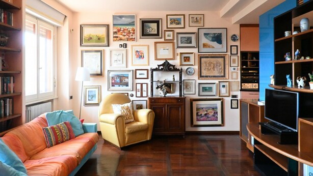 A living room with a sofa, armchair, and a wall decorated with framed pictures.