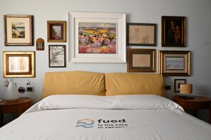 A hotel room with a bed, framed artwork on the walls, and a logo on the bedspread.