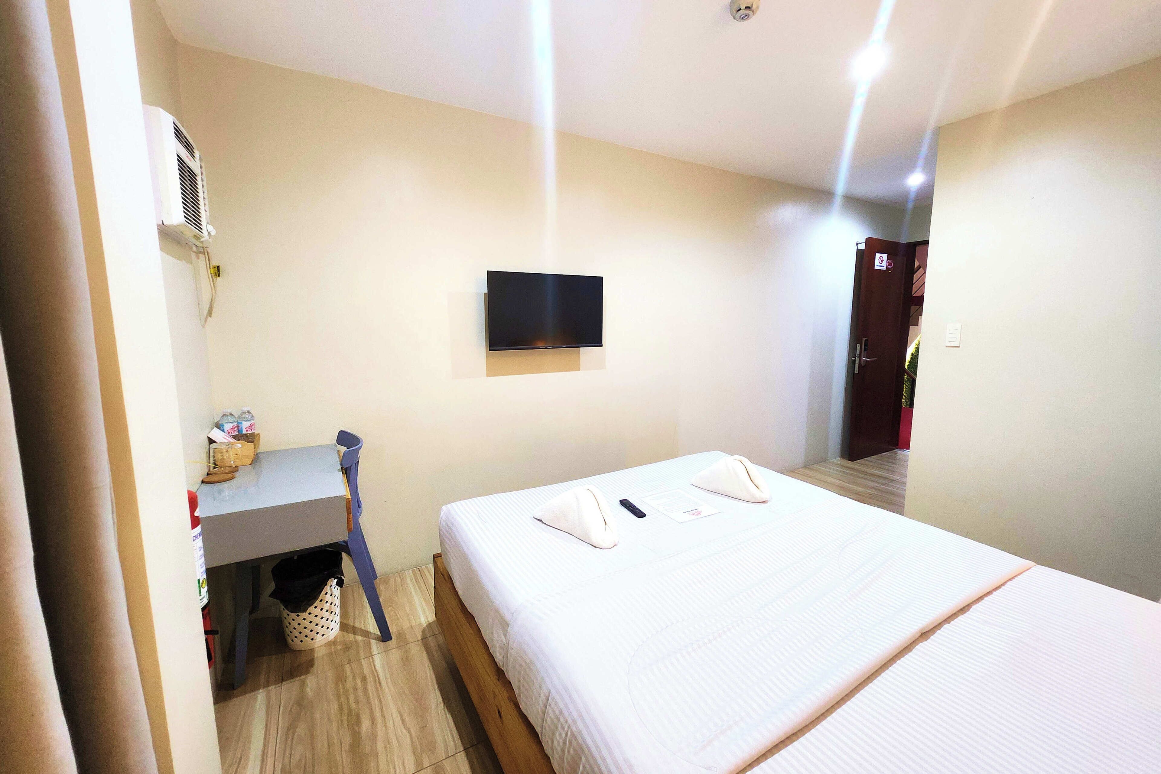 A hotel room with a bed, a desk, a television, and an air conditioning unit.