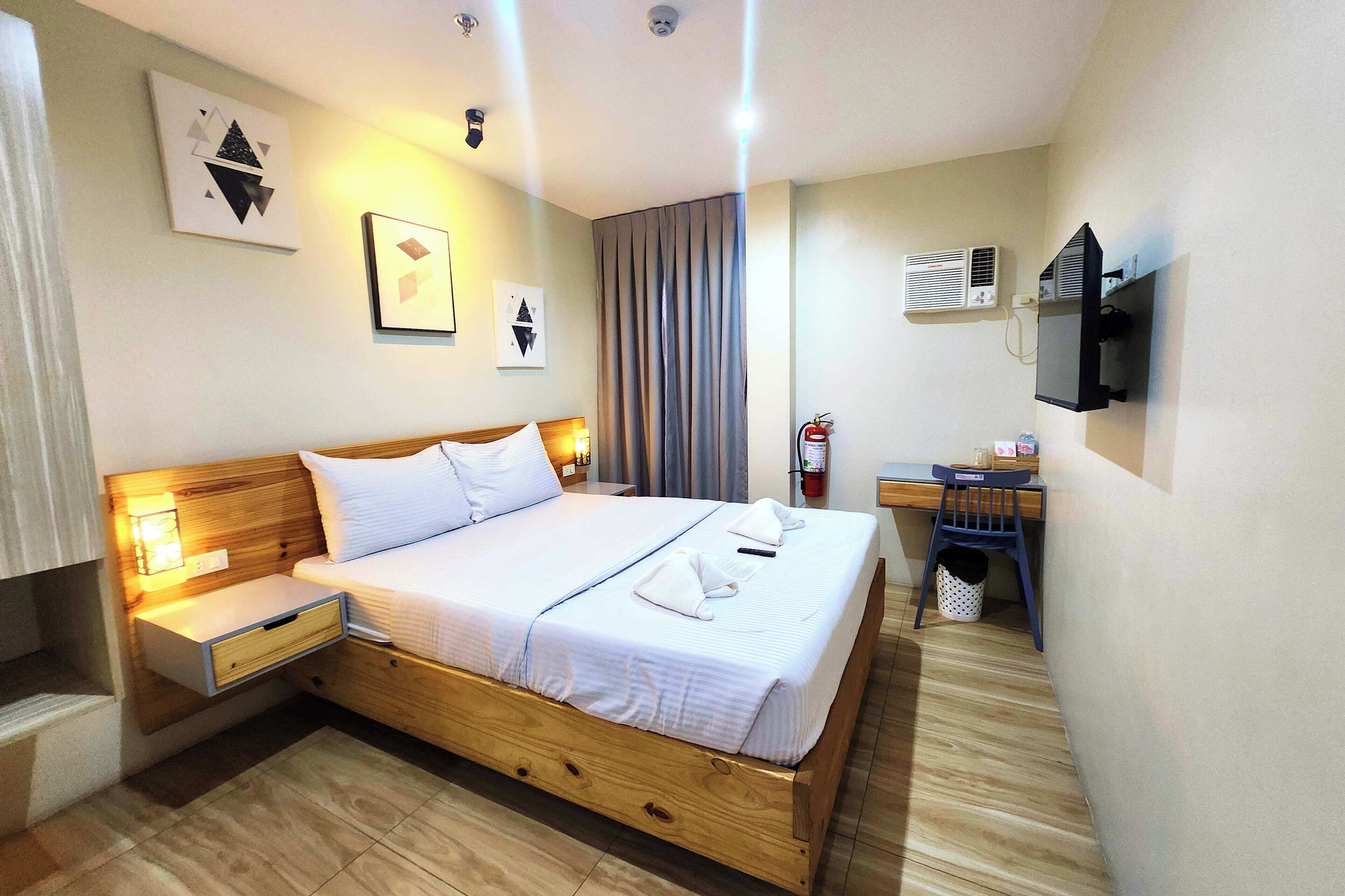 A hotel room with a wooden bed, bedside tables, a desk, and a television.