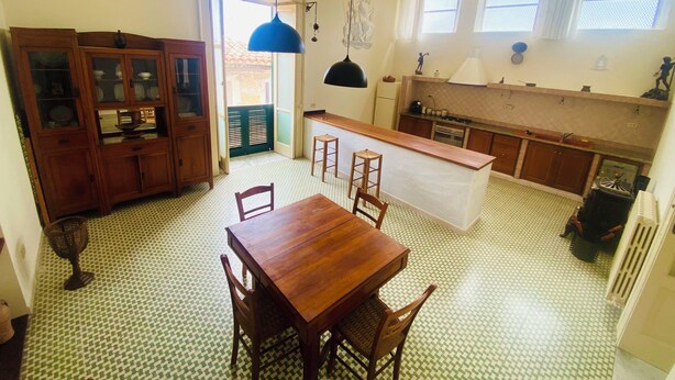 A compact kitchen with a dining area, featuring a wooden table and chairs, a built-in cabinet, and a hanging light fixture. - Domus Evora - Period home in the historic center (Tropea)