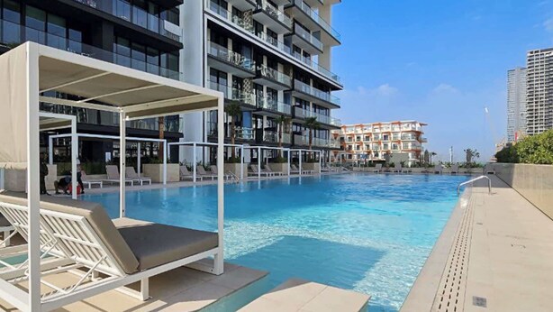 A swimming pool with lounge chairs and a covered seating area. - StayShort - JVC Apartment Sleeps 4 with Pool View! (JVC)