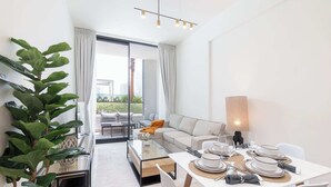 A modern living room with a glass dining table set for four, a sofa, and a large plant. - StayShort - JVC Apartment Sleeps 4 with Pool View! (JVC)