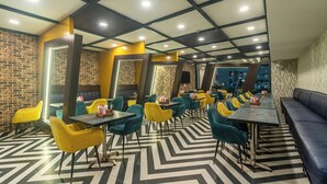 A restaurant with a modern interior, featuring a black and white chevron floor pattern, yellow and teal chairs, and a brick wall on one side. - Treebo Viennahttps://apps.expediapartnercentral.com/ (Jaipur)
