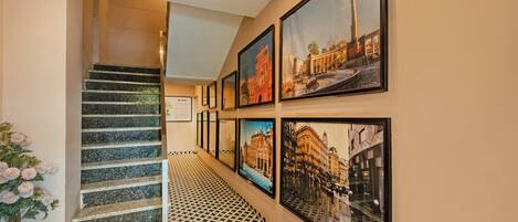 A hallway with a staircase, patterned floor, and framed pictures on the wall.