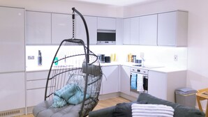 A modern kitchen with white cabinets, a hanging chair, and a small dining area. - Birmingham City centre apartments (Birmingham)