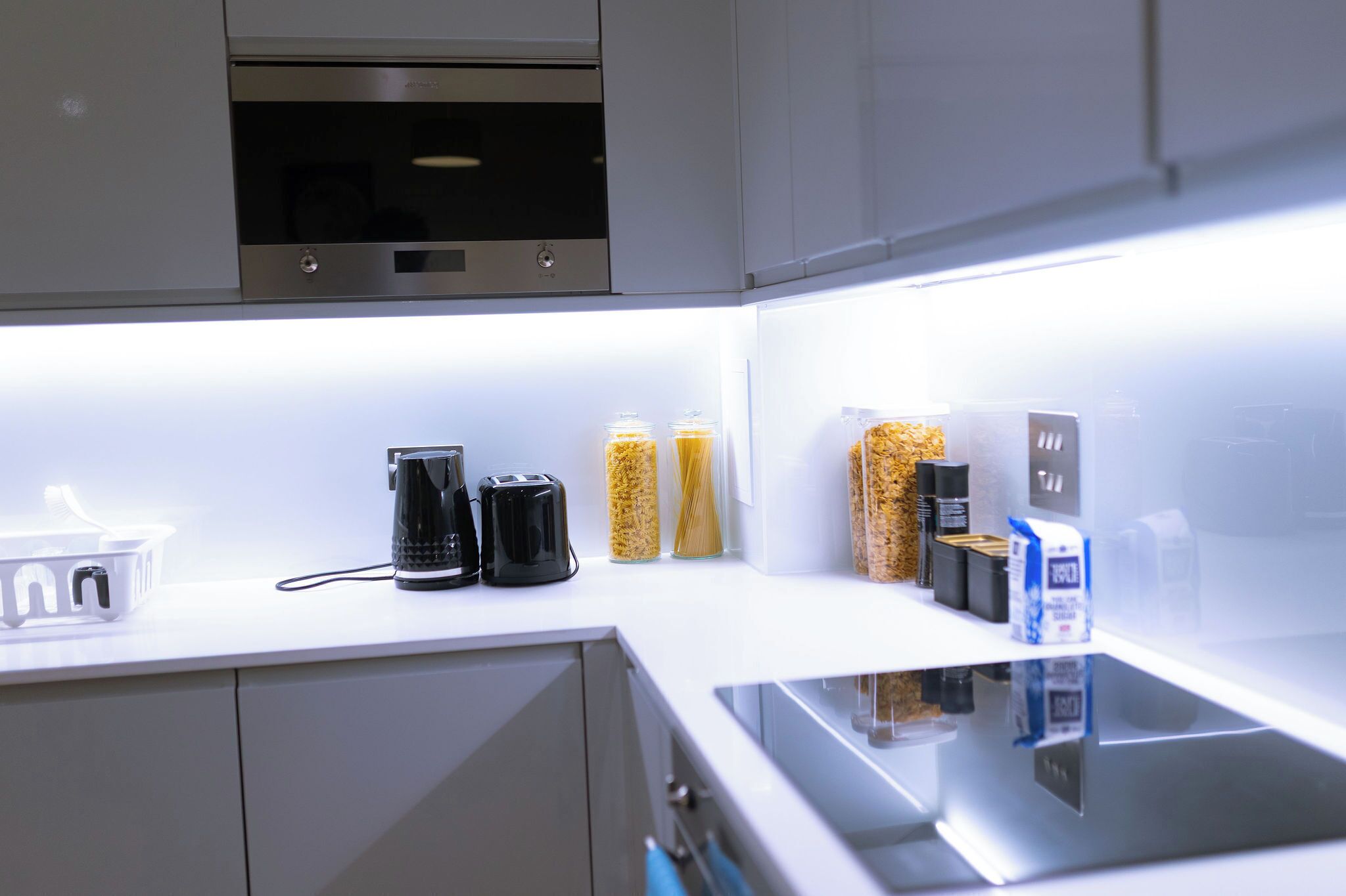 Eine moderne Küche mit Einbauofen, Kaffeemaschine, Gläsern mit Pasta und einer Milchpackung.
