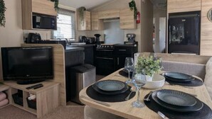 A compact RV interior with a kitchenette, a dining area with a table set for two, and a television. - Casita De Cuervo at Country Park (Lymington)