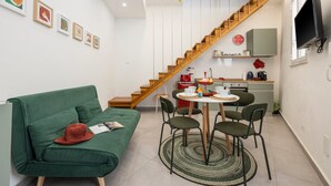 A modern interior with a green sofa, a dining table with chairs, a kitchen area, and a wooden staircase.