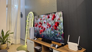 A living room with a flat-screen TV, a wooden entertainment unit, a plant, and a wall-mounted speaker.