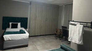 A hotel room with a bed, a desk, a chair, and a bathroom with a towel rack.