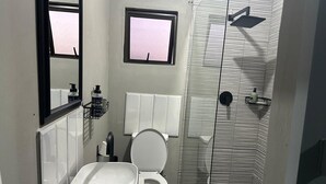 A compact bathroom with a white sink, toilet, and a shower area with a glass door.