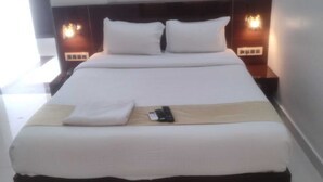 A neatly made bed with white linens, a wooden headboard, and bedside lamps. - Hotel Itagi Square (Vijayapura)