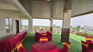 A conference room with green artificial grass, red and yellow chairs, and a long table. - Hotel Itagi Square (Vijayapura)