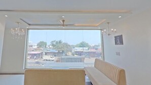A modern room with a large window, a ceiling fan, and a sofa. - Hotel Itagi Square (Vijayapura)