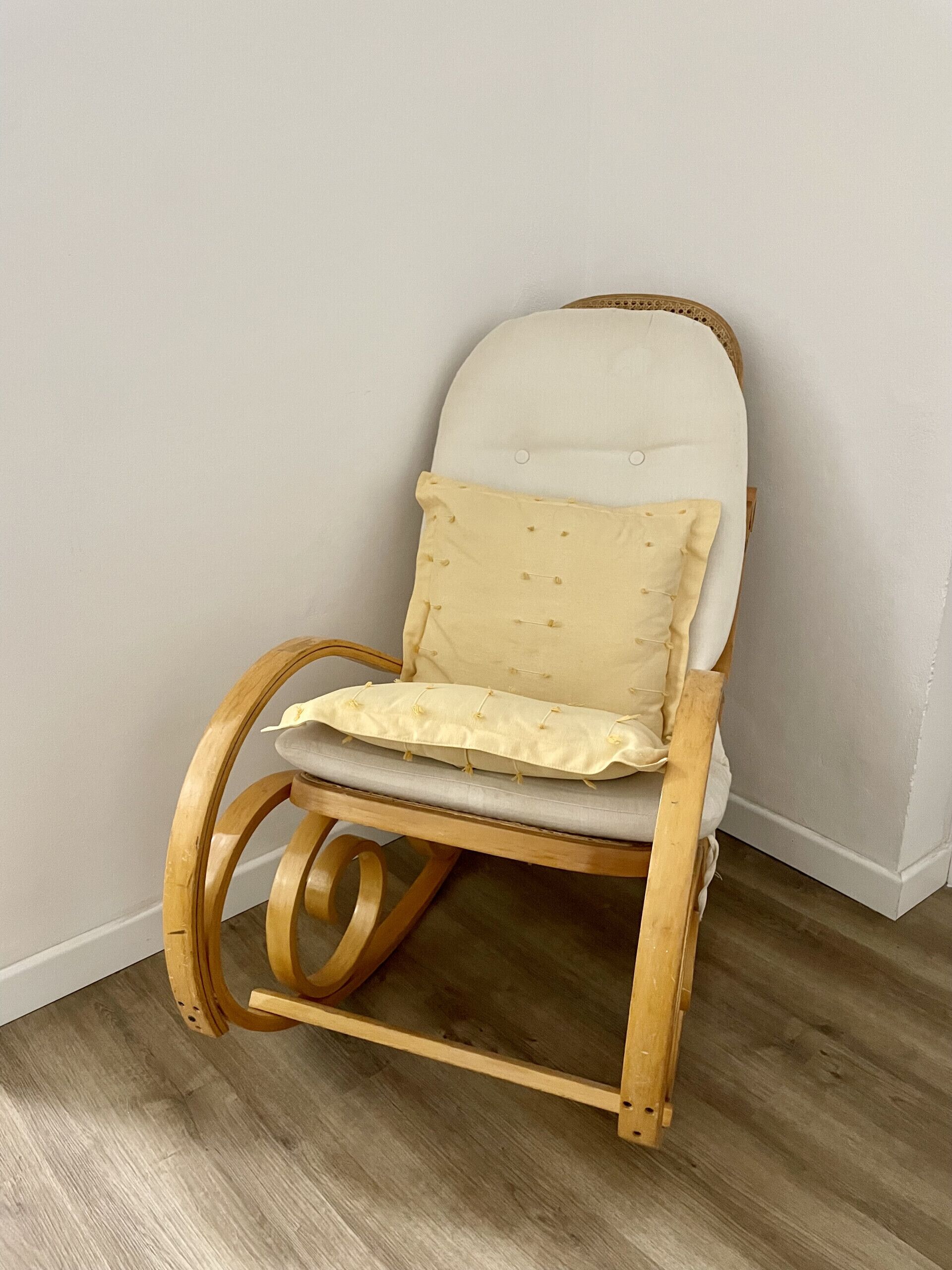 A wooden rocking chair with a white cushion and a beige pillow.