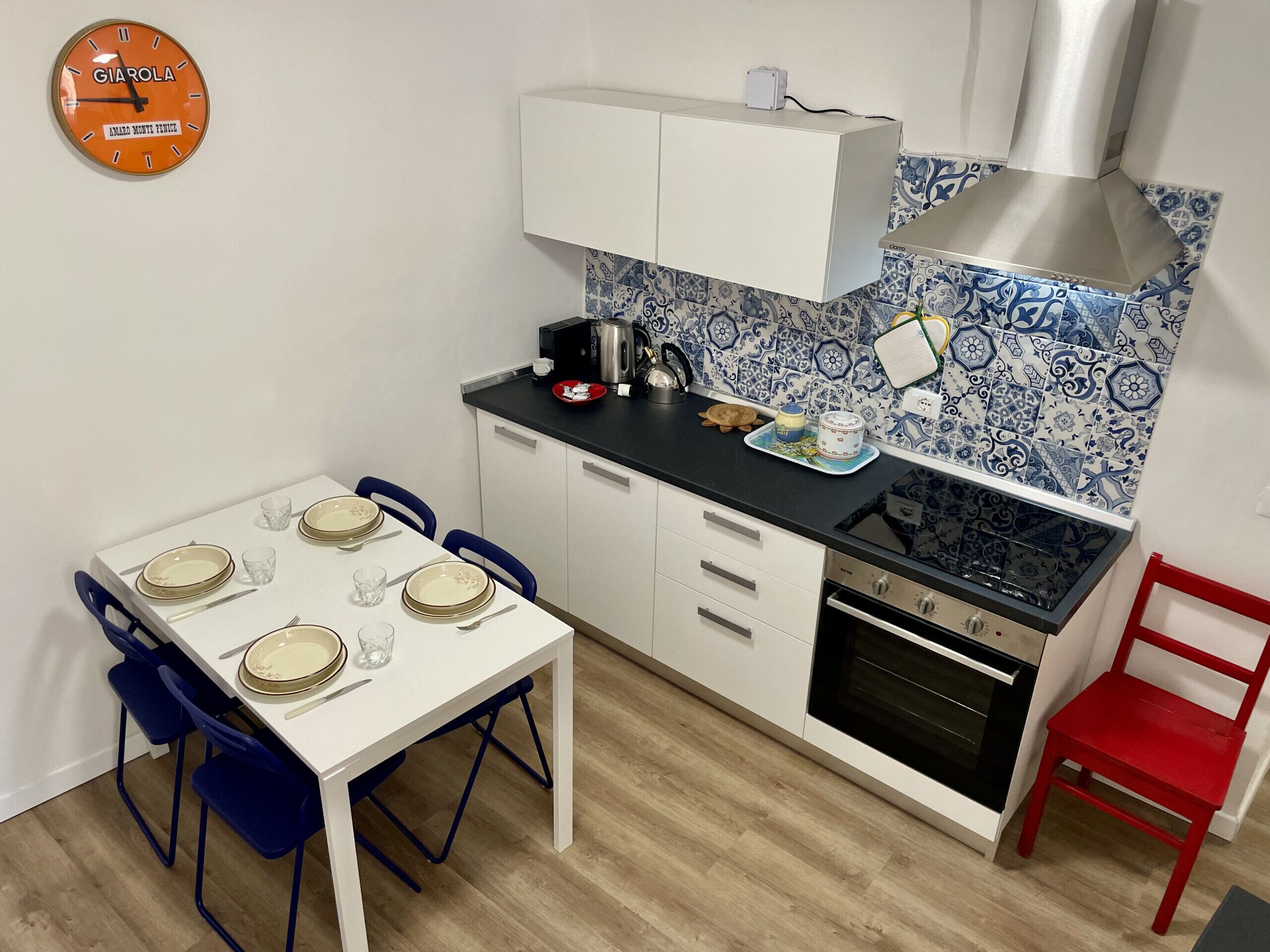 Cocina compacta con una mesa blanca preparada para cuatro personas, estufa y una silla roja.