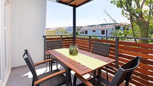Ein Balkon mit Holztisch und -stühlen, einem Blumentopf und Blick auf Häuser im Hintergrund.