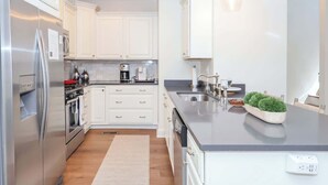 Une cuisine moderne avec des meubles blancs, des appareils en acier inoxydable, un plan de travail noir et une petite plante d’intérieur.