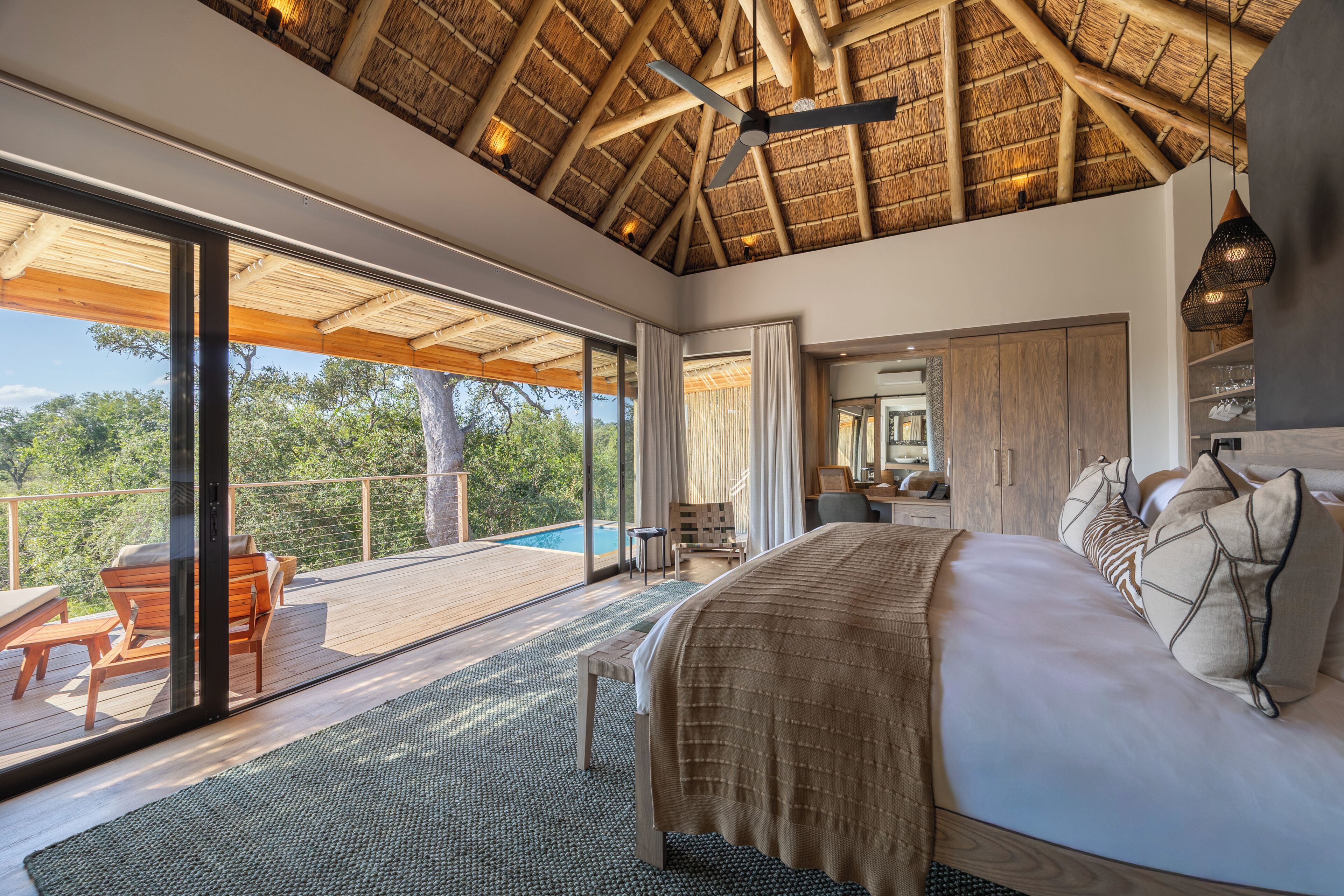 A bedroom with a large bed, a ceiling fan, and a view of the outdoors.