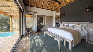 A bedroom with a large bed, a desk, a chair, and a view of a swimming pool. - Klaserie Drift Amani (Klaserie Private Nature Reserve)
