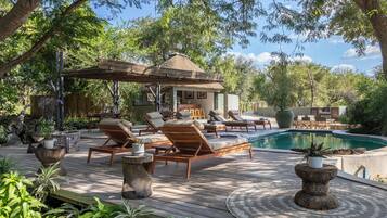 A wooden deck with lounge chairs, a pool, and a gazebo.