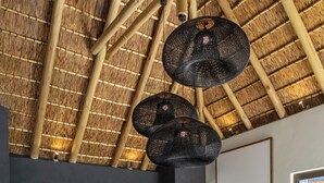 A room with a thatched ceiling, a sofa, two armchairs, a coffee table, and artwork on the walls. - Klaserie Drift Amani (Klaserie Private Nature Reserve)