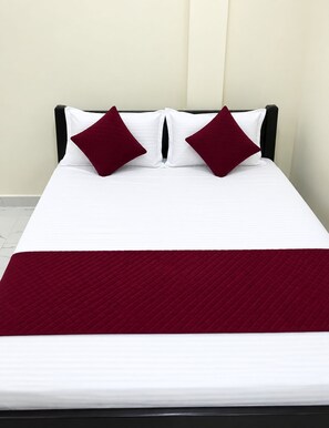 Una cama con sábanas blancas, dos almohadas rojas, un cabecero oscuro y una manta roja.