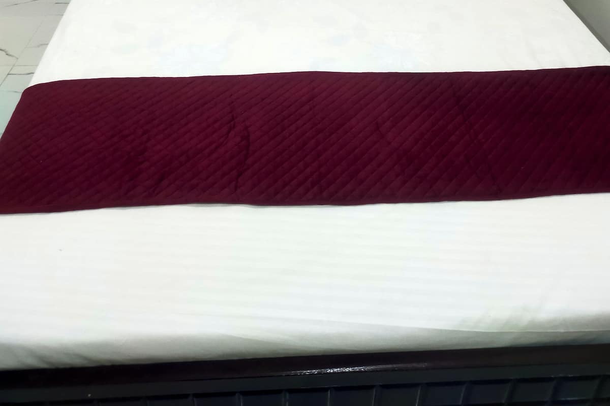 Een bed met wit beddengoed en twee donkerrode kussens.