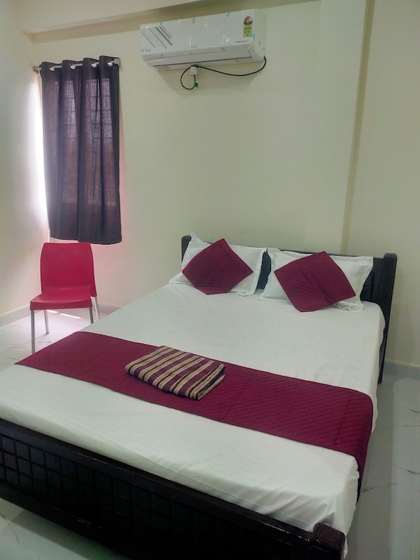 Une chambre d’hôtel avec un lit, une chaise rouge, une fenêtre avec des rideaux et un appareil de climatisation fixé au mur.