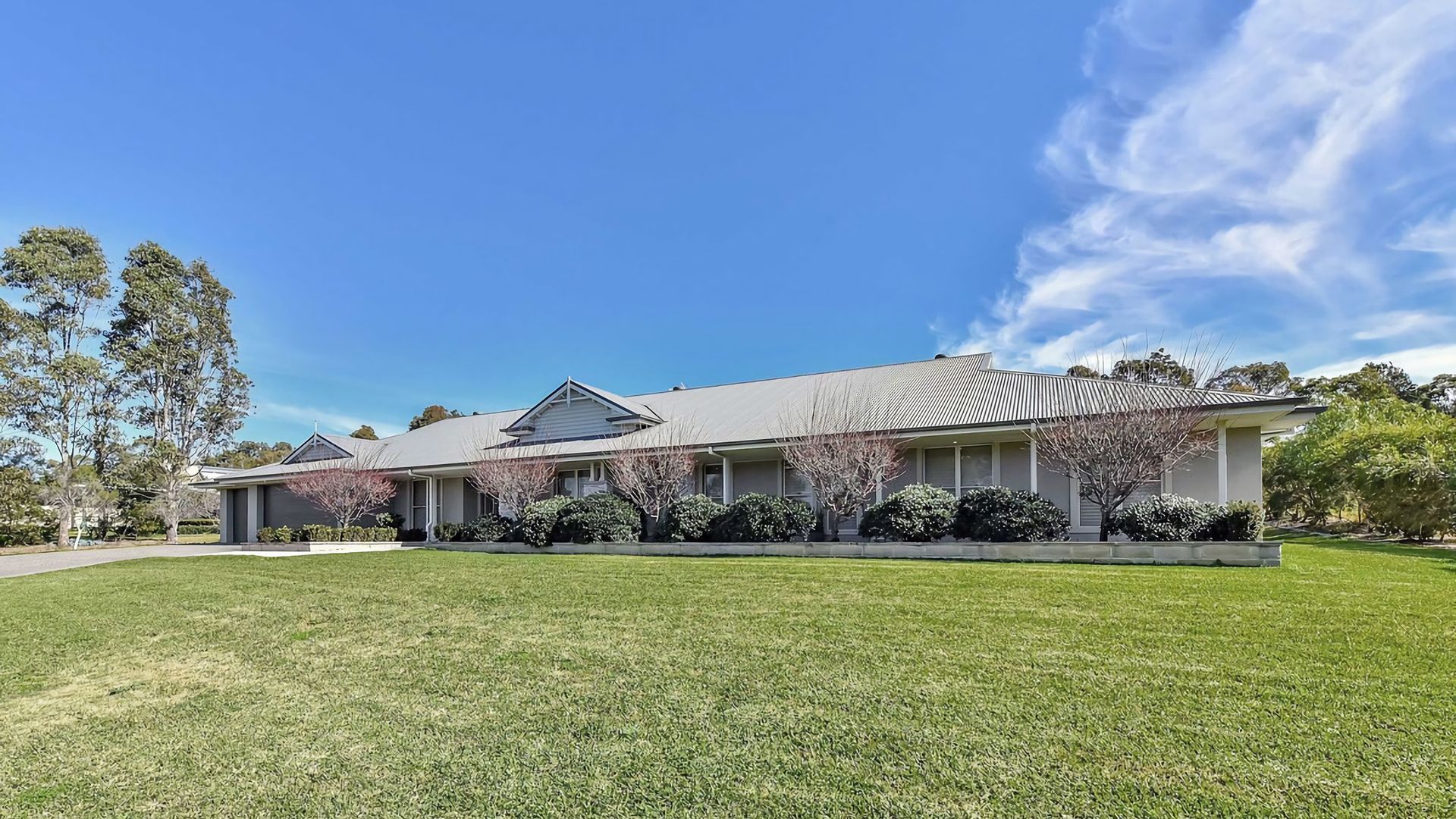 A two-story residential building with a flat roof, a front lawn, and mature trees.