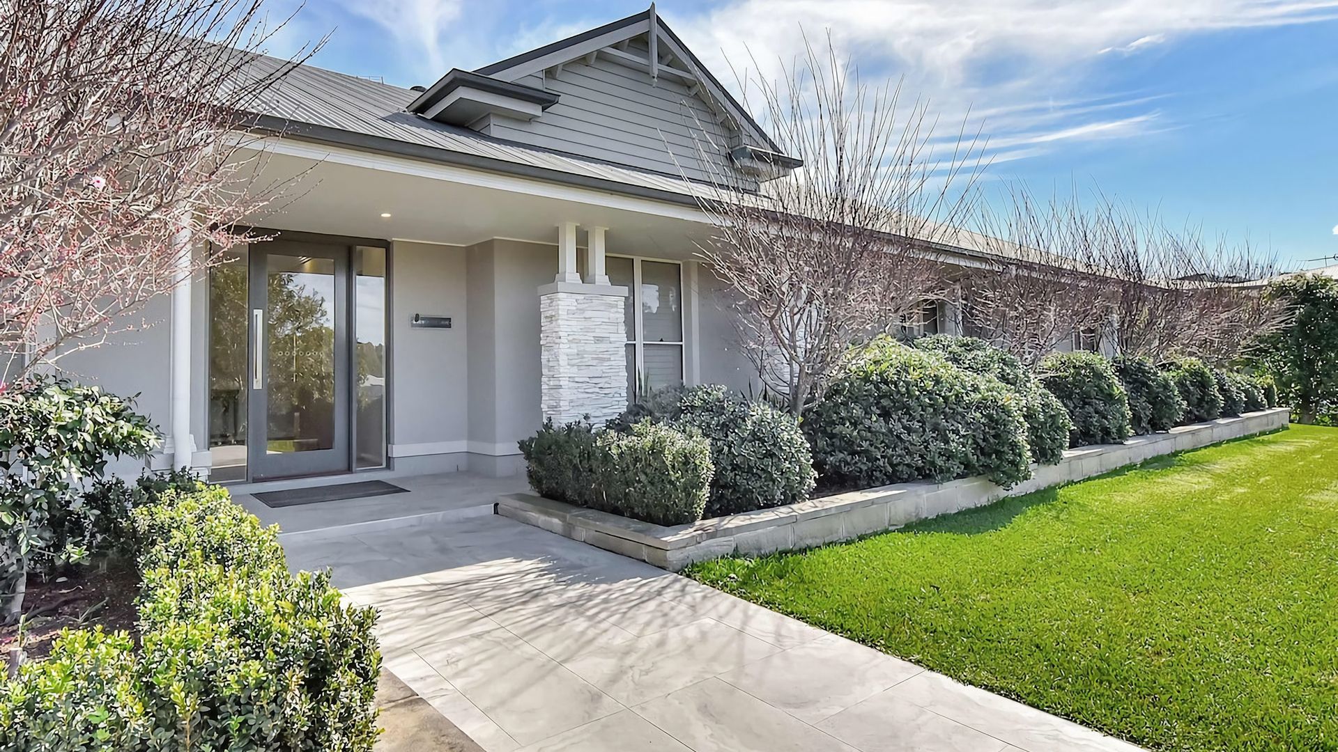 A modern two-story building with a stone facade, a covered entrance, and a well-maintained lawn.