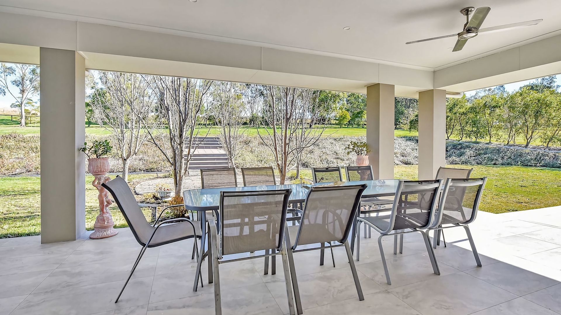 An outdoor patio with a table and chairs, a ceiling fan, and a view of a landscaped garden.