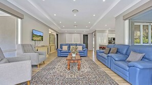 A spacious living room with a blue sofa set, a grey armchair, and a patterned rug.