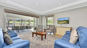 A spacious living room with a large sofa set, a coffee table, and a television mounted on the wall.