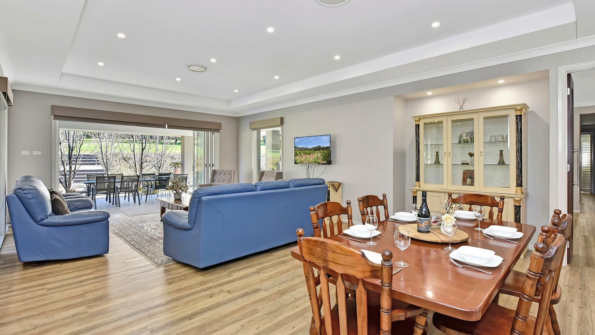 A modern living room with a blue sofa, dining table set for six, and a large cabinet with glass doors.